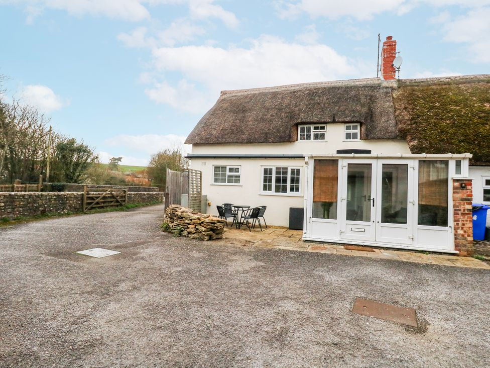 A cottage with a thatched roof and outdoor seating area at Long Barn, Burton Bradstock