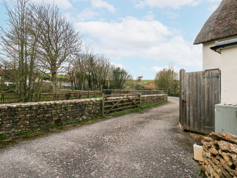 A gravel road with a stone wall and trees at Long Barn in Burton Bradstock