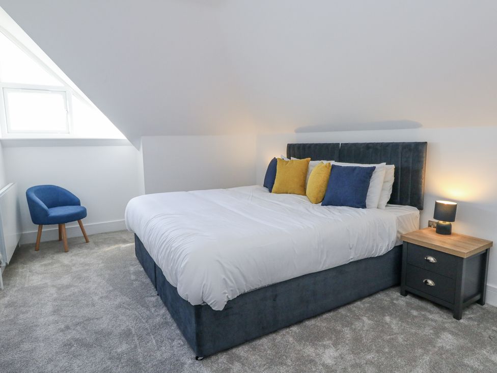 A bedroom with a bed, pillows, nightstand, and an armchair at Seafern House 36B in Poole