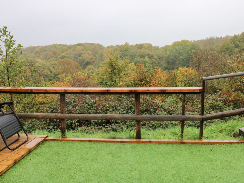 A terrace with a green surface and wooden railing overlooking a forest at Cwtch Bach Aberdare