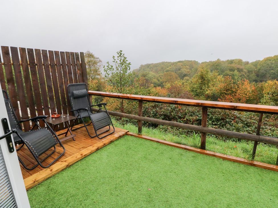 An outdoor area with chairs and a table overlooking a forest at Cwtch Bach in Aberdare