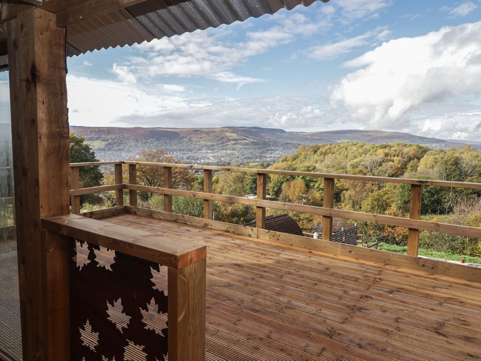 An outdoor deck with wooden railing and view of mountains at Cwtch Bach Aberdare