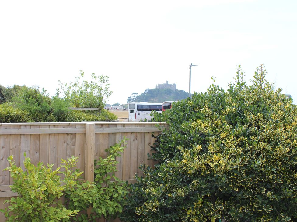 A view of a hill with a castle and a bus behind a fence at Sea Whispers in Marazion