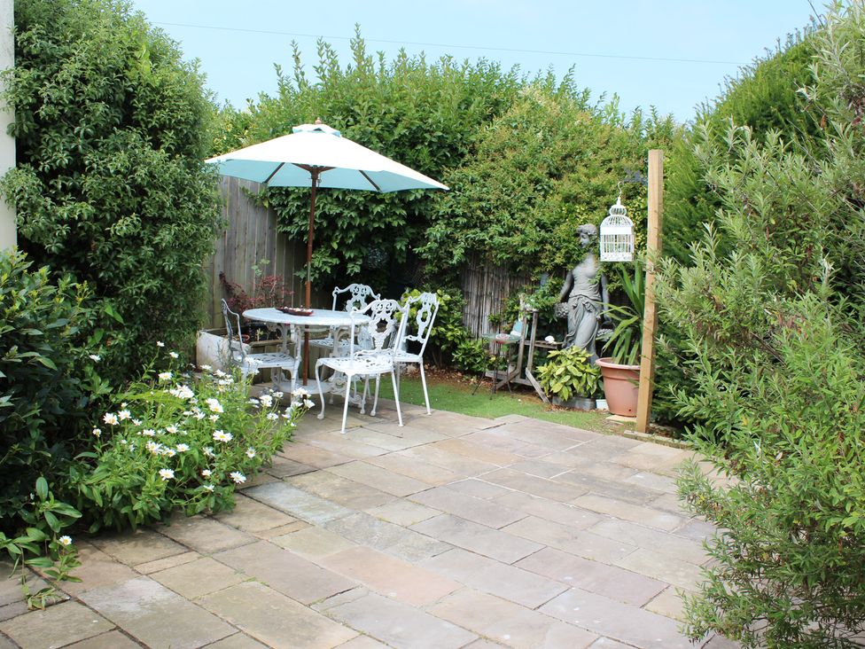 A garden with a table and chairs under a parasol at Sea Whispers in Marazion