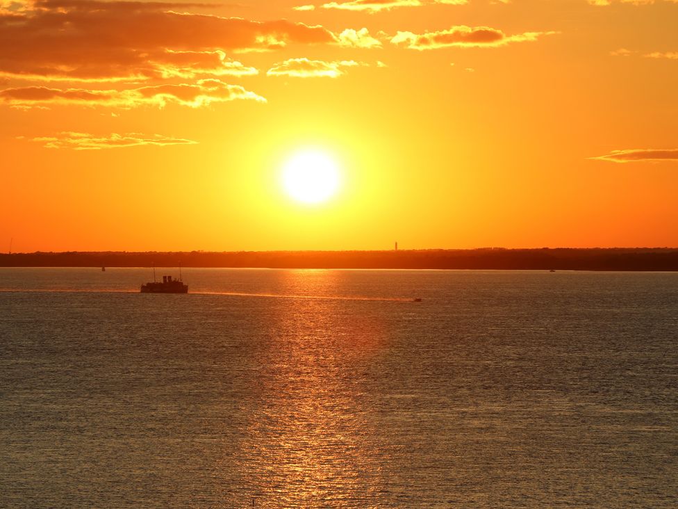 A sunset over the ocean with a boat visible at The Bookshop Apartment in Cowes