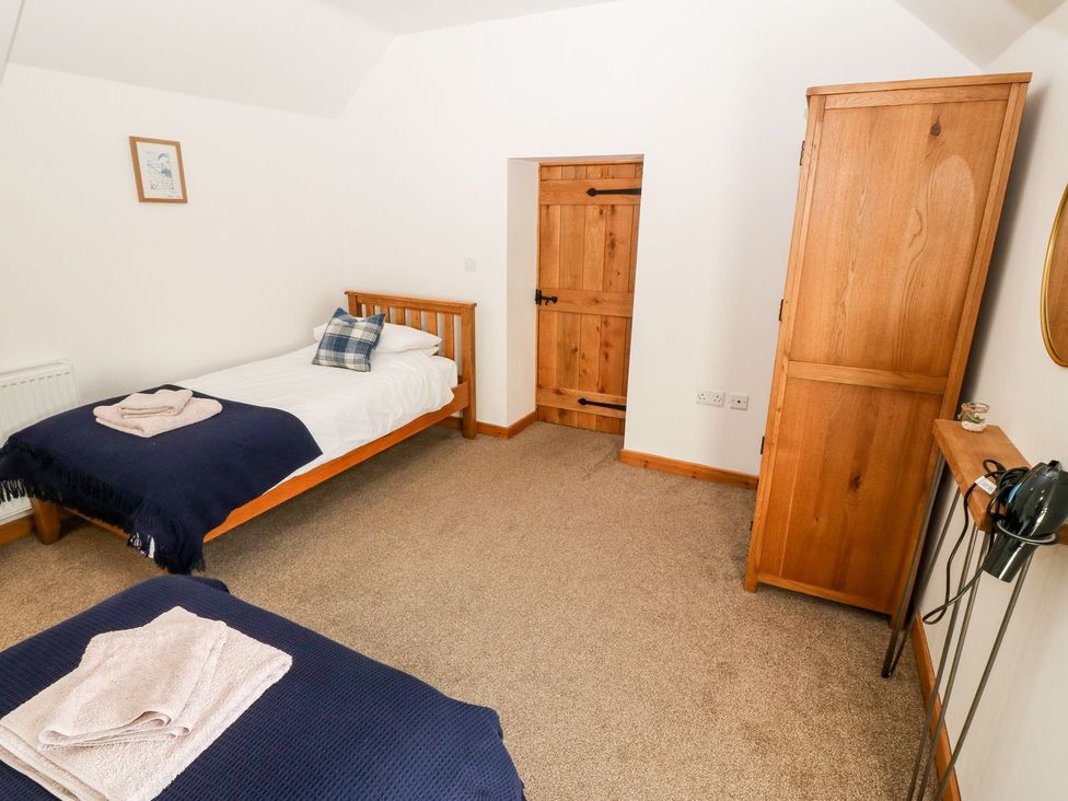 A bedroom with two beds and a wardrobe at The Old Barn in Pwllheli