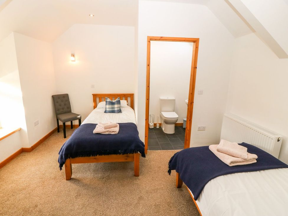 A bedroom with two beds and a bathroom access at The Old Barn in Pwllheli