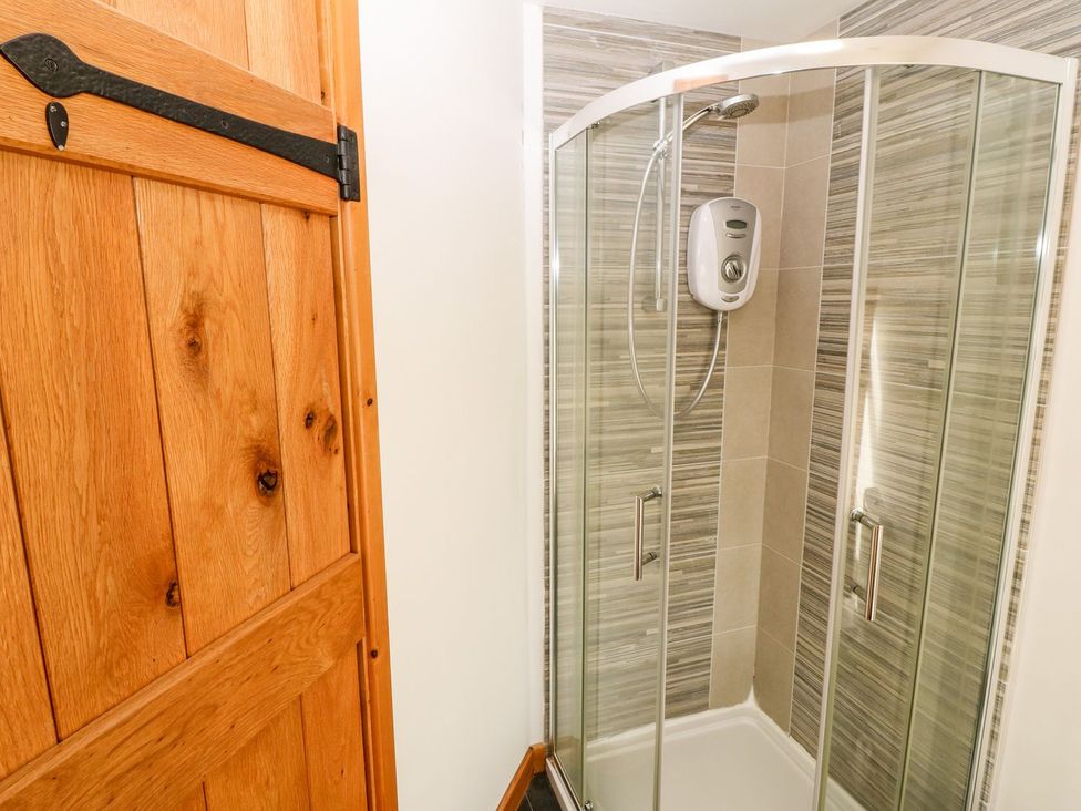 A shower unit with glass doors and wooden door at  in Pwllheli