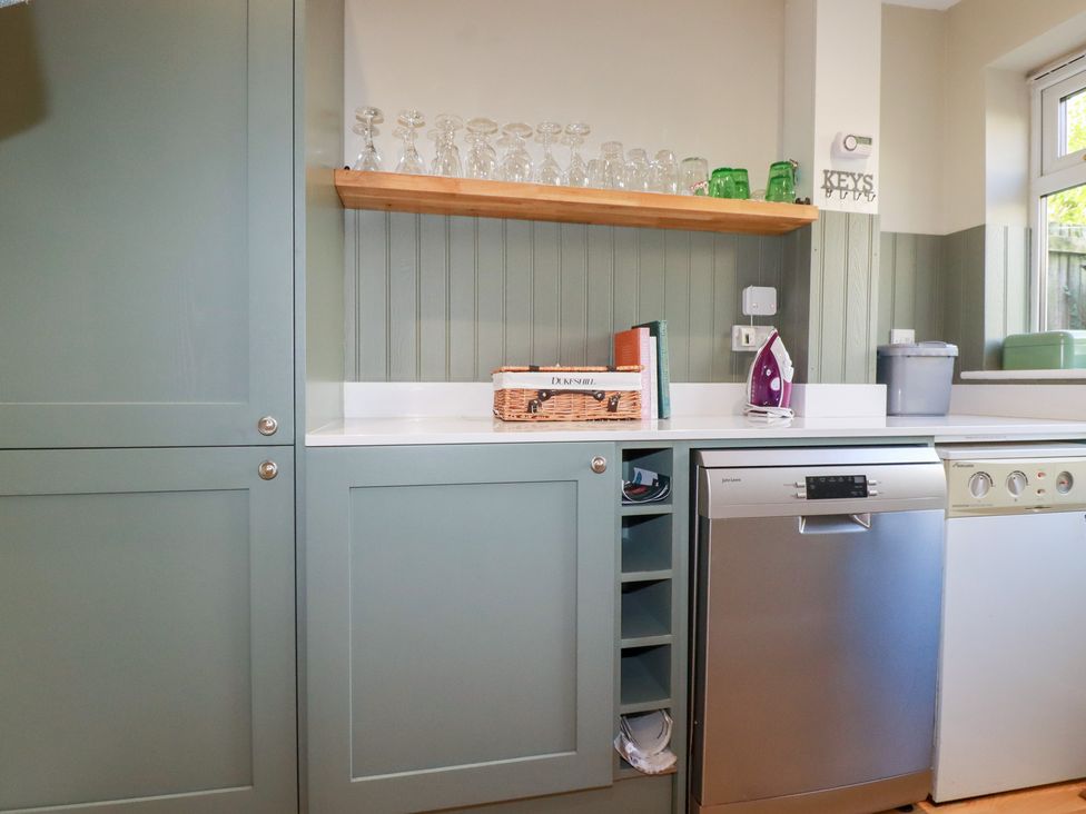 A kitchen with cabinets, glasses on a shelf, and a dishwasher at The Mizzen St Endellion near Port Isaac