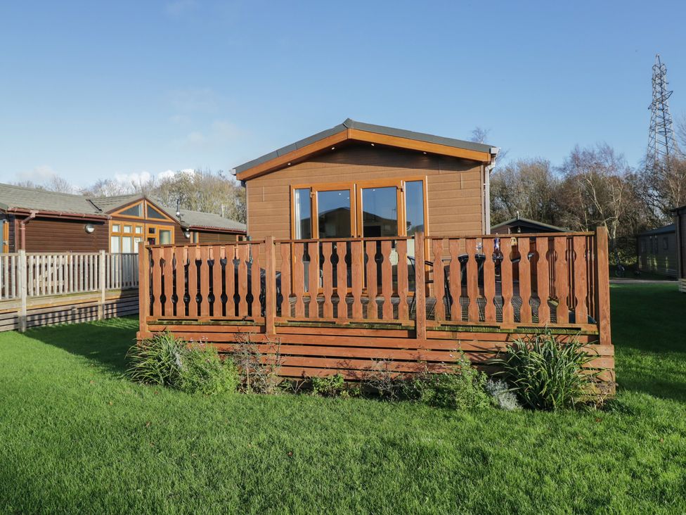A cabin with a deck and grass area at Bluebell Lodge in Warton