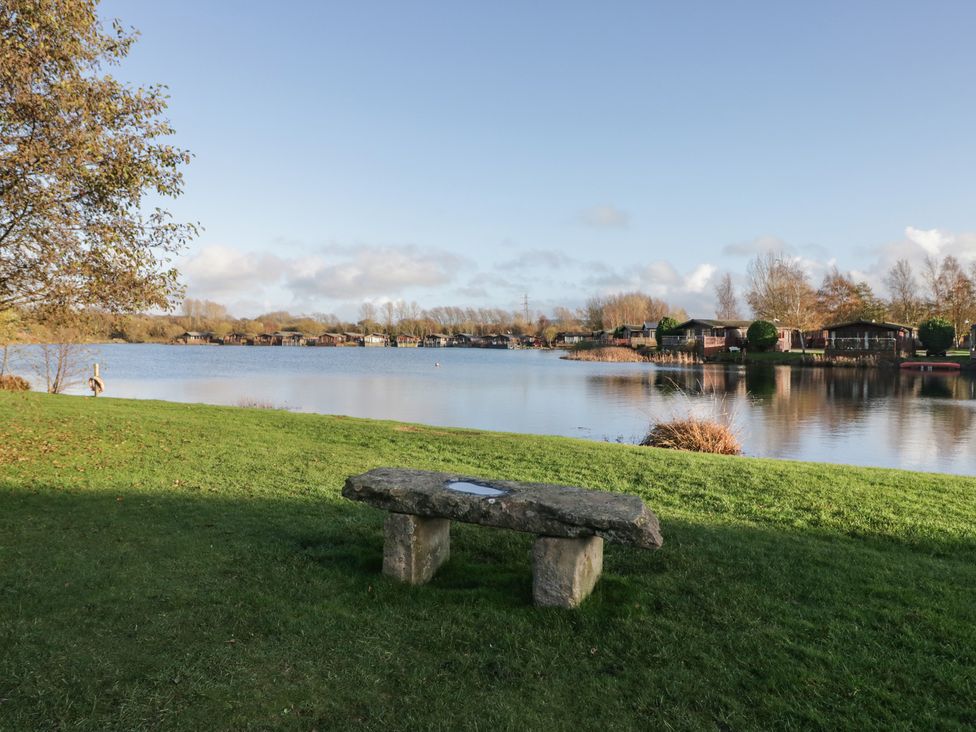 A lake with a stone bench and trees at Bluebell Lodge in Warton