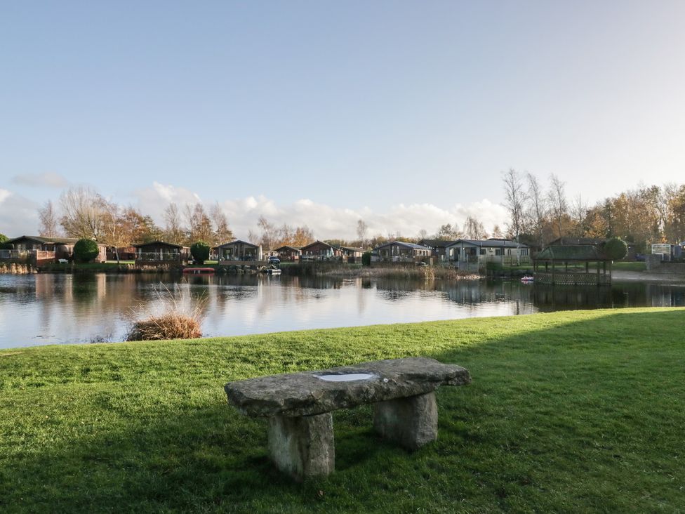 A view of cabins by a lake with a stone bench at Bluebell Lodge in Warton