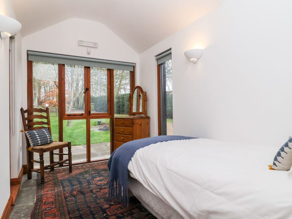A bedroom with a bed, chair, and mirror at Owl Cottage in Woodbridge