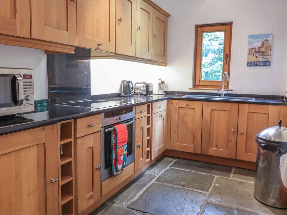 A kitchen with wooden cabinets and appliances at Owl Cottage in Kettleburgh near Framlingham
