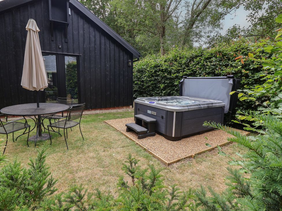A garden with a hot tub, table and chairs at Owl Cottage in Kettleburgh near Framlingham
