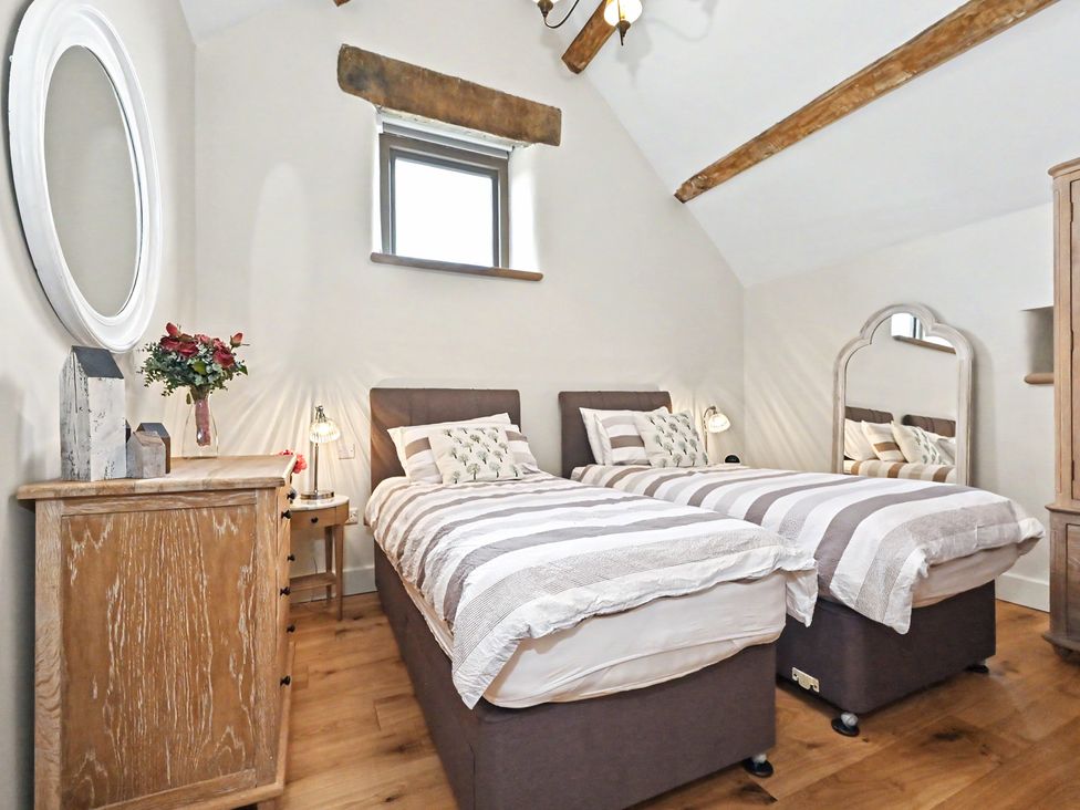 A bedroom with twin beds and a mirror at Lane House Farm Barn Butterton