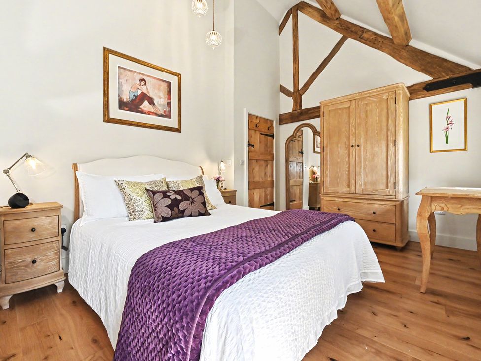 A bedroom with a bed, bedside table, and wardrobe at Lane House Farm Barn Butterton