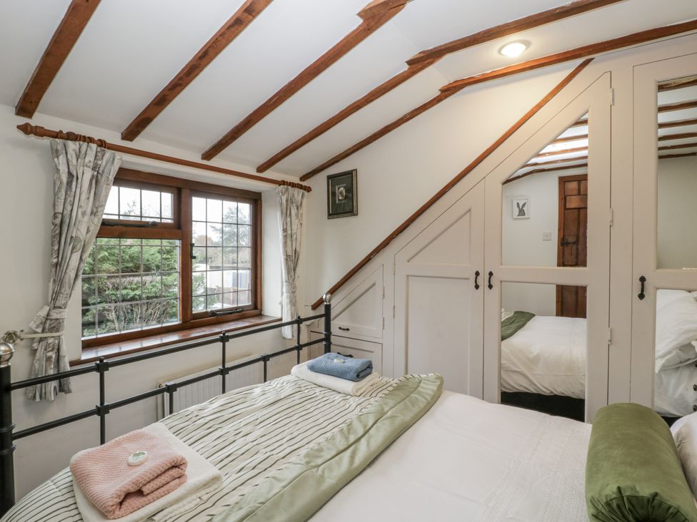 A bedroom with a bed, curtains and a wardrobe at Magpie Cottage in Worcester