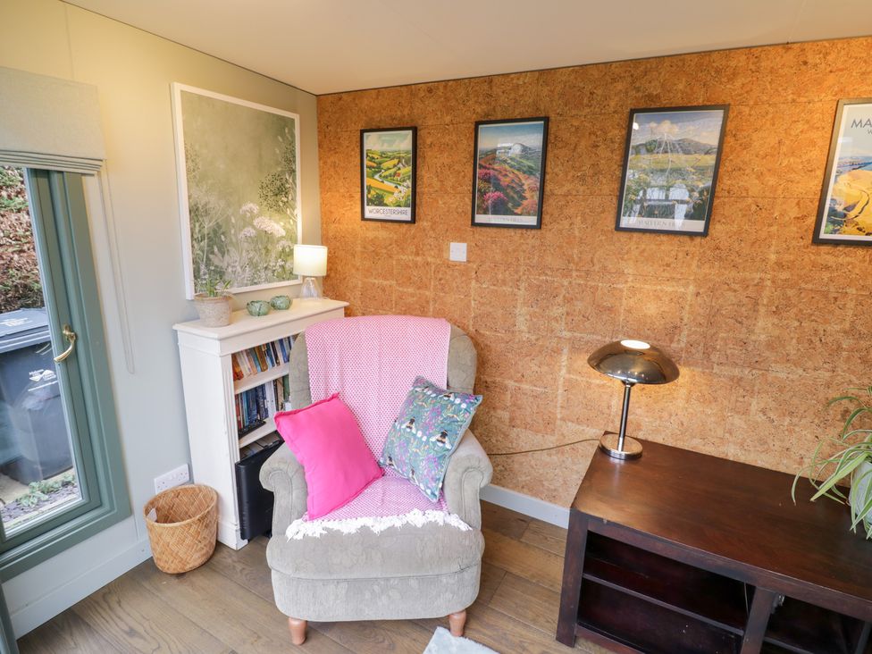 A snug with an armchair and bookshelf at Magpie Cottage Powick near Callow End