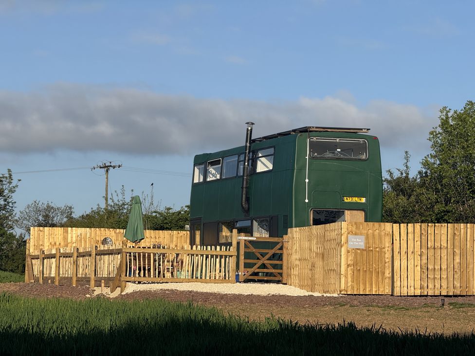 A green bus with a fence and outdoor seating at The Bus on the Hill, Huntsham near Bampton, Devon