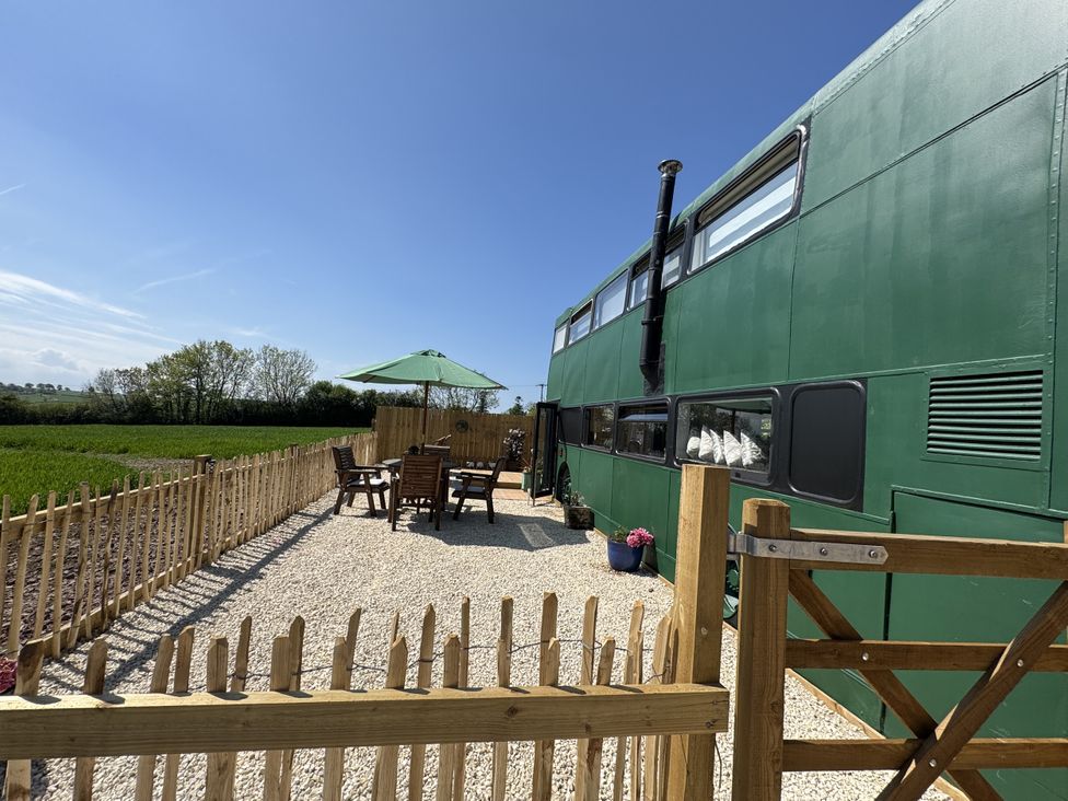 An outdoor area with a green bus, table and chairs at The Bus on the Hill in Huntsham near Bampton, Devon