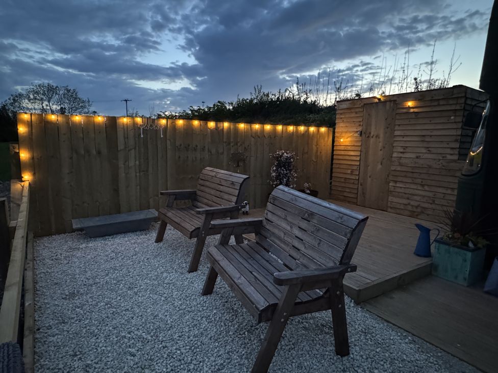 An outdoor area with wooden chairs and gravel surface at The Bus on the Hill in Huntsham near Bampton, Devon