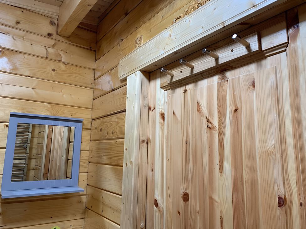 A bathroom with a wood wall, mirror, and hooks at Duncairin cabins