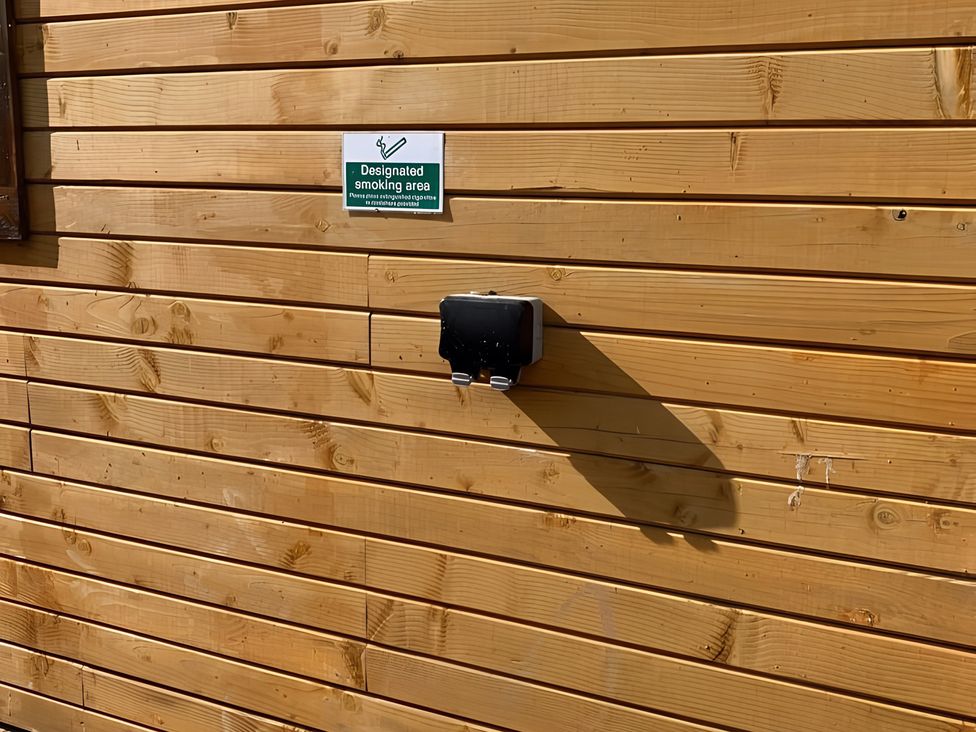 A wooden wall with a designated smoking area sign and an ashtray at Duncairin cabins