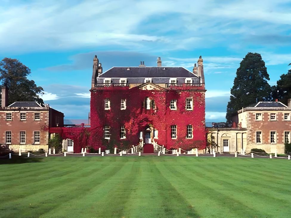 A large building with red ivy on the facade and a lawn at Duncairin cabins