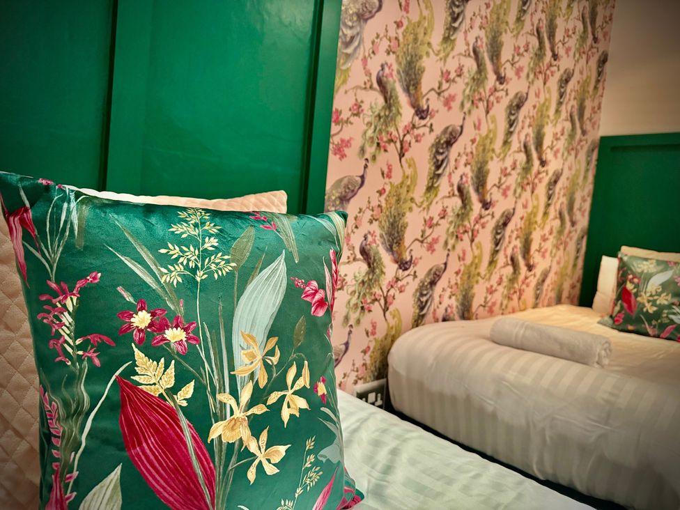 A bedroom with floral pillows and patterned wallpaper at Horncliffe Hot Tub House