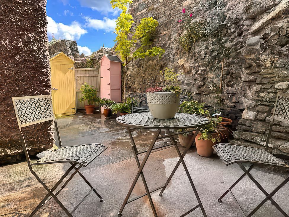 A garden with a table and chairs beside potted plants at Periwinkle Cottage in Conwy