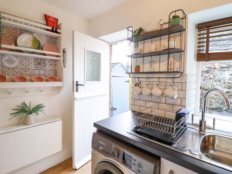 A kitchen with a sink and plates on a shelf at Periwinkle Cottage in Conwy