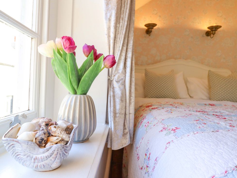 A bedroom with a bed and flowers on a table at Periwinkle Cottage in Conwy