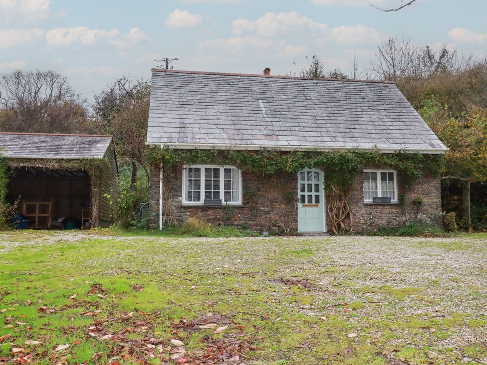 A cottage with a blue door and windows surrounded by grass and trees at Copper Mine Cottage in Bodmin
