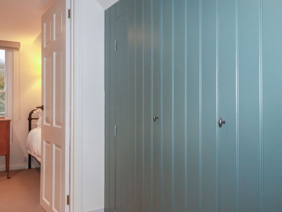 A bedroom with a door, dresser, window and wardrobe at Copper Mine Cottage in Bodmin
