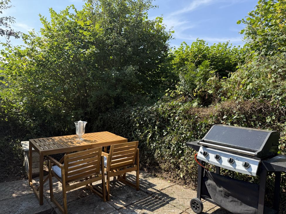 A garden with a table and chairs next to a grill at Copper Mine Cottage in Trelill near Port Isaac