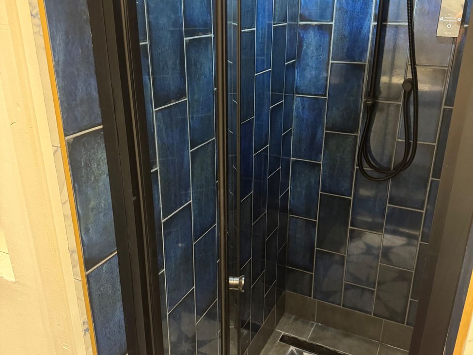 A shower enclosure with blue tiles and a showerhead at a bathroom