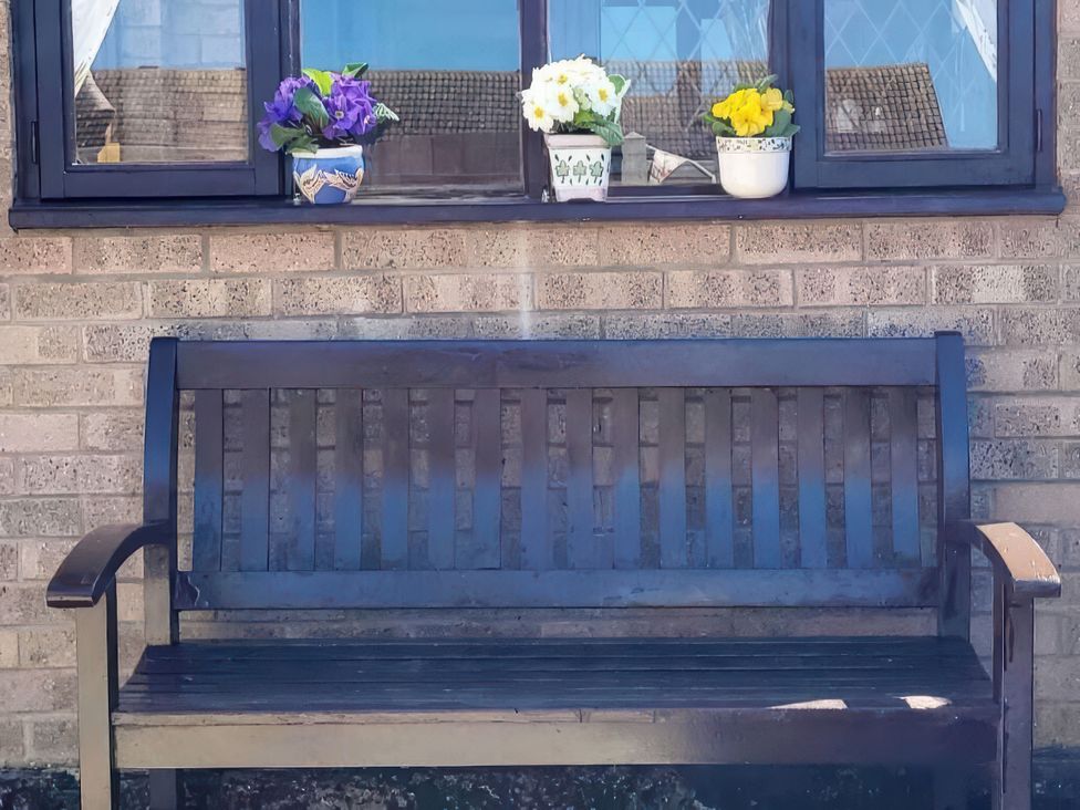 A bench under a window with flower pots at Quackers Heacham