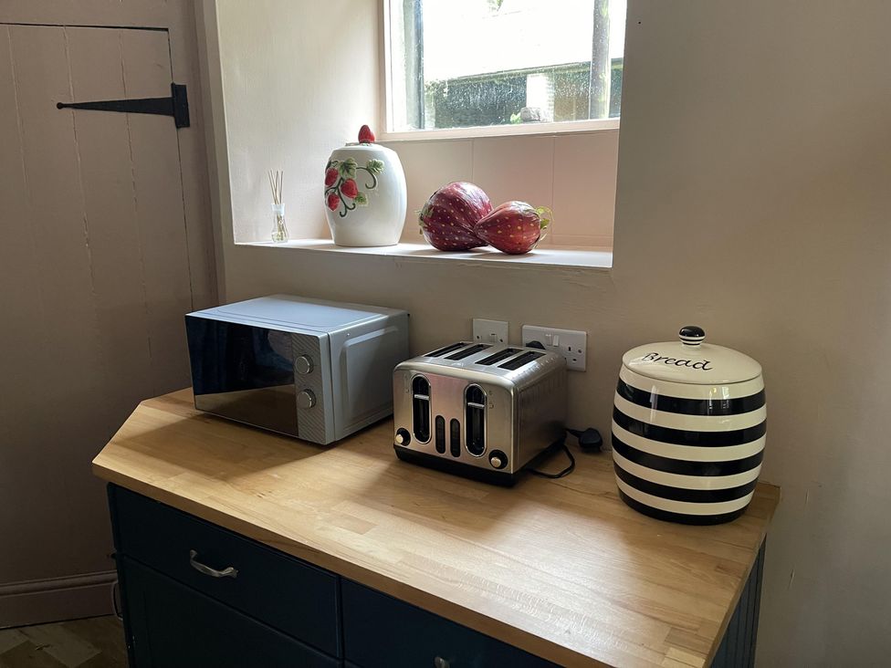 A kitchen countertop with a microwave, toaster, and bread bin at High Dyke Cottage
