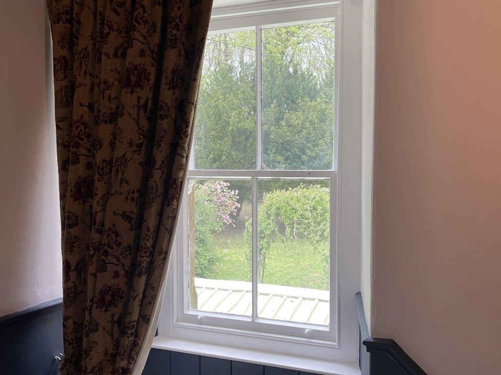A window with a curtain showing greenery outside at High Dyke Cottage