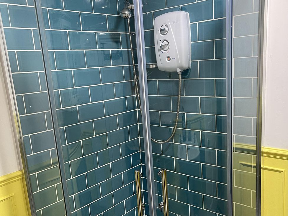 A shower with glass doors and blue tiled walls at High Dyke Cottage