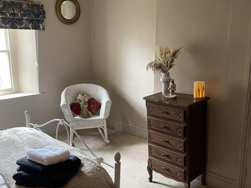 A bedroom with a bed, dresser, chair, and decorative flowers at High Dyke Cottage