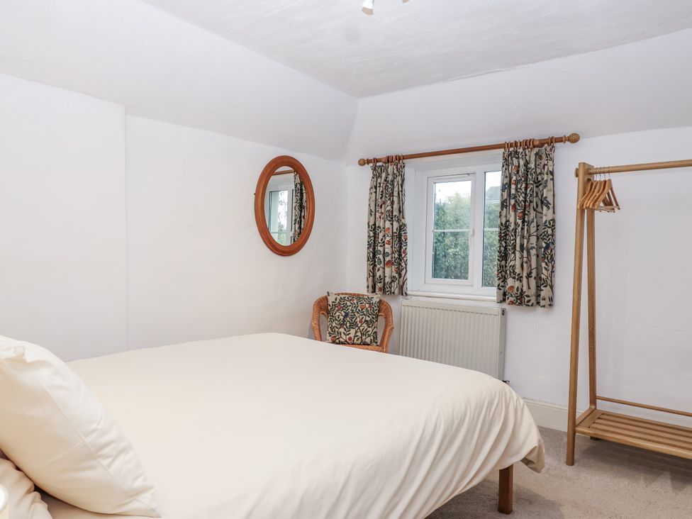 A bedroom with a bed, chair, mirror, and window at Orchard Cottage Dawlish