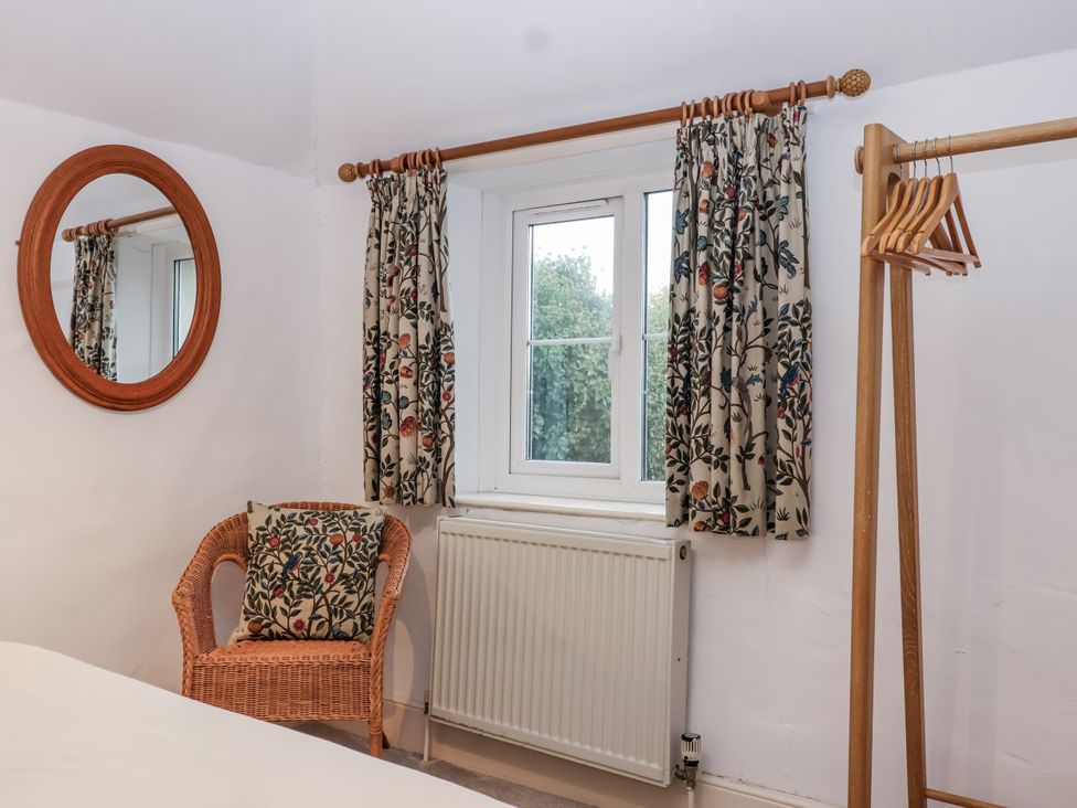 A bedroom with a mirror and a chair at Orchard Cottage in Dawlish