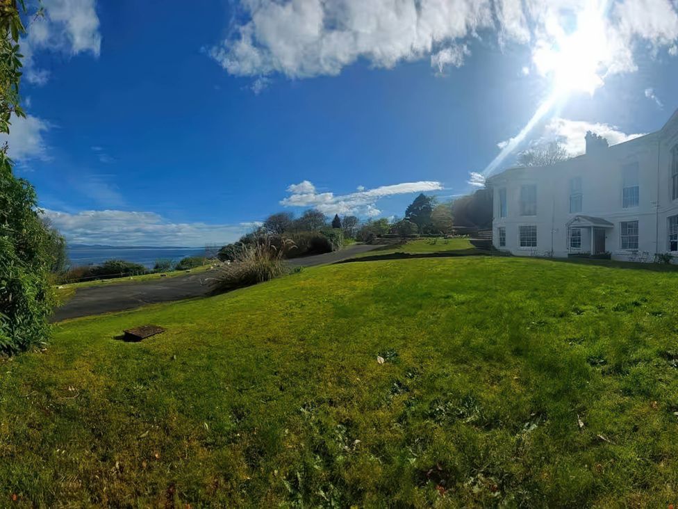 An outdoor view of a lawn and house near the ocean with a blue sky