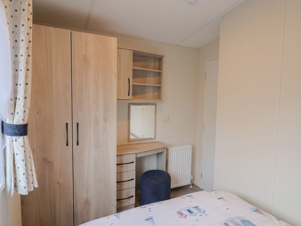 A bedroom with a wardrobe, desk, mirror, and chair at caravan NEW in Uplyme