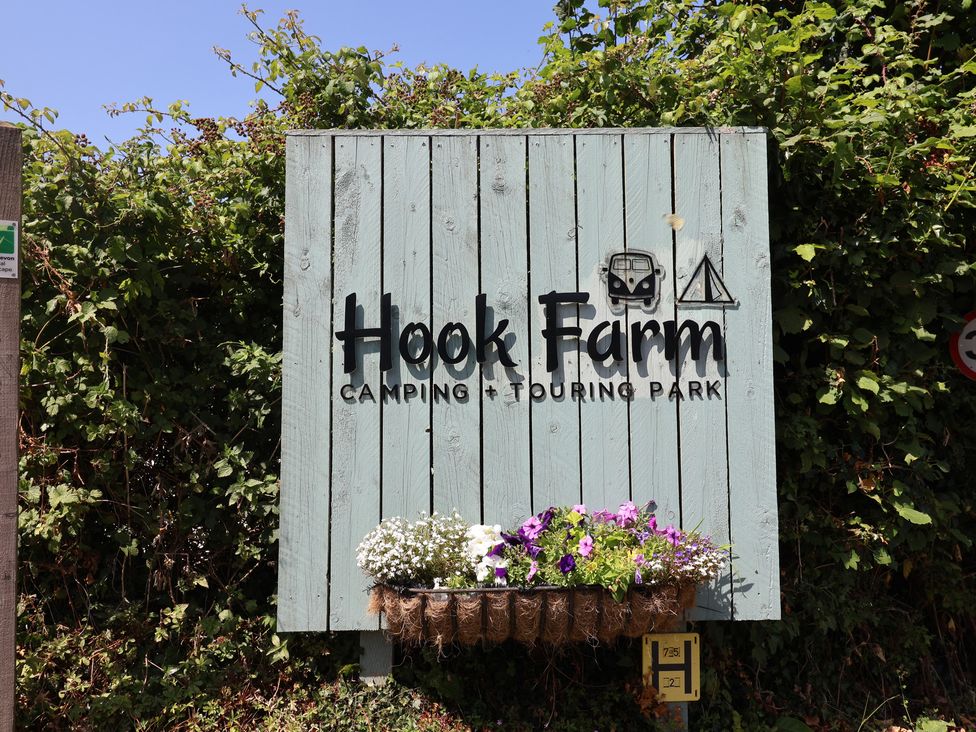 A sign for Hook Farm Camping and Touring Park with flowers at Uplyme