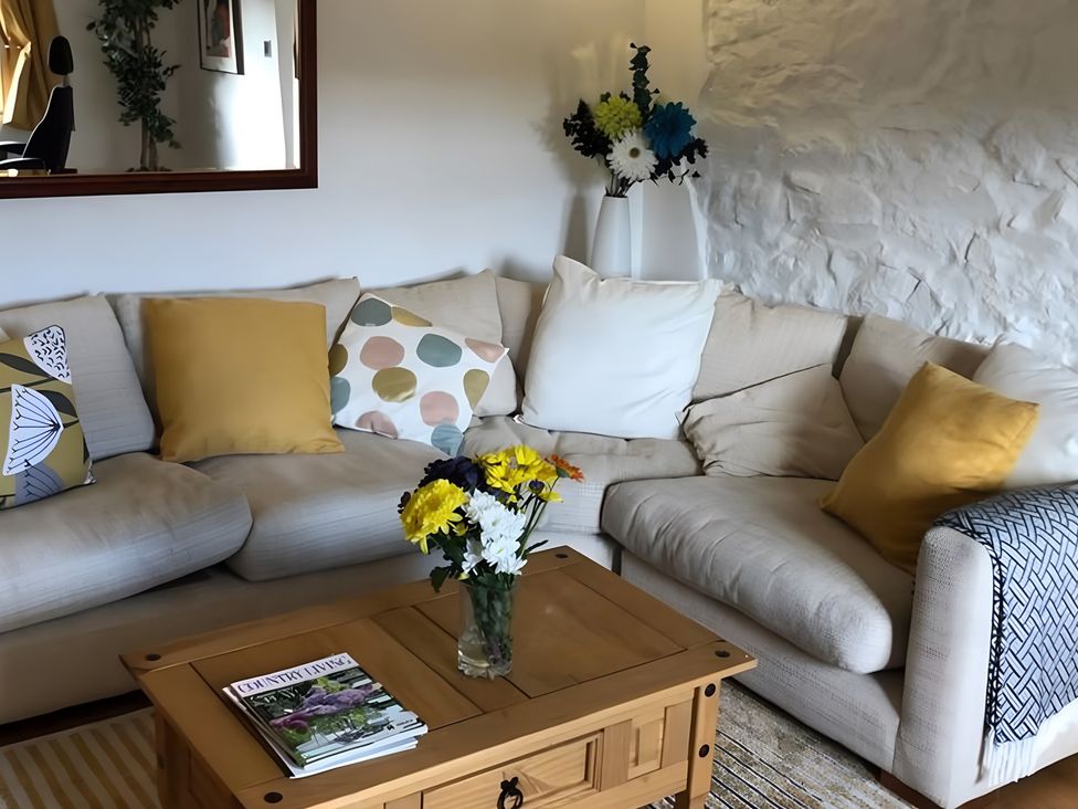 A living room with a sofa and coffee table featuring flowers at Tranquil Cottage 