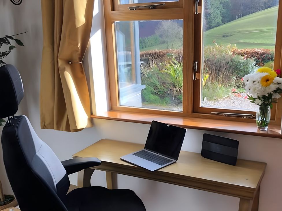 An office with a laptop on a table and flowers by the window at Tranquil Cottage