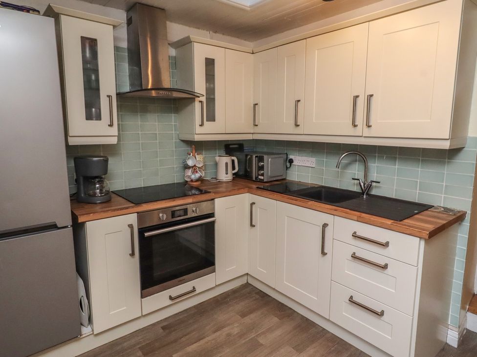 A kitchen featuring a refrigerator, oven, sink, coffee maker, and cabinets at Corner Cottage in Seahouses